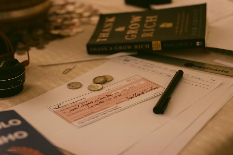 Real estate investing paperwork with coins, check, pen, and the book "Thank and Grow Rich" on a desk.