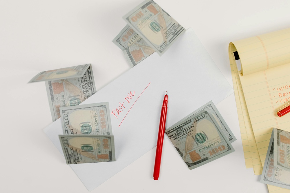 Envelope labeled "Past Due" with scattered $100 bills and a red pen on a desk