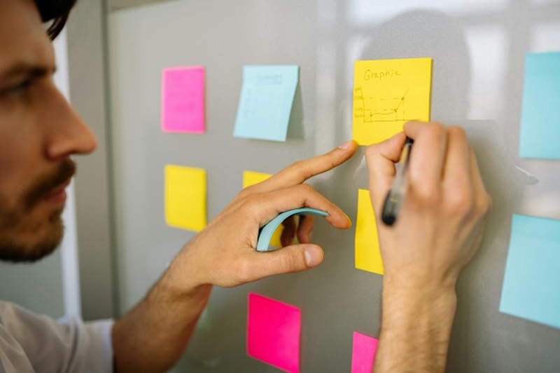 Person writing on sticky notes while planning a credit evaluation strategy on a whiteboard