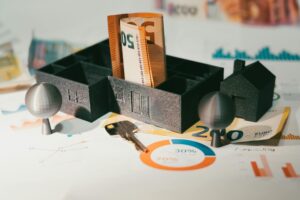 Miniature houses with euro banknotes and financial charts illustrating real estate investing, mortgage notes, and the impact of interest rates on returns and cash flow.